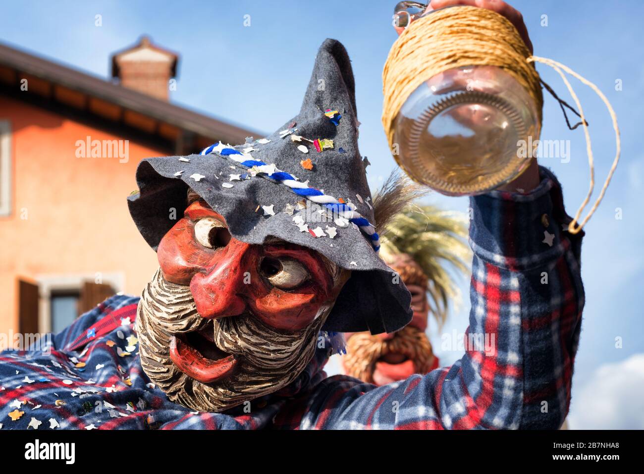 Porträt eines maskierten Mannes, der eine leere Weinflasche hält. Fröhlicher betrunkener Mann in traditioneller heidnischer Tracht. Karnevalsumzug von Pust. Italien. Stockfoto