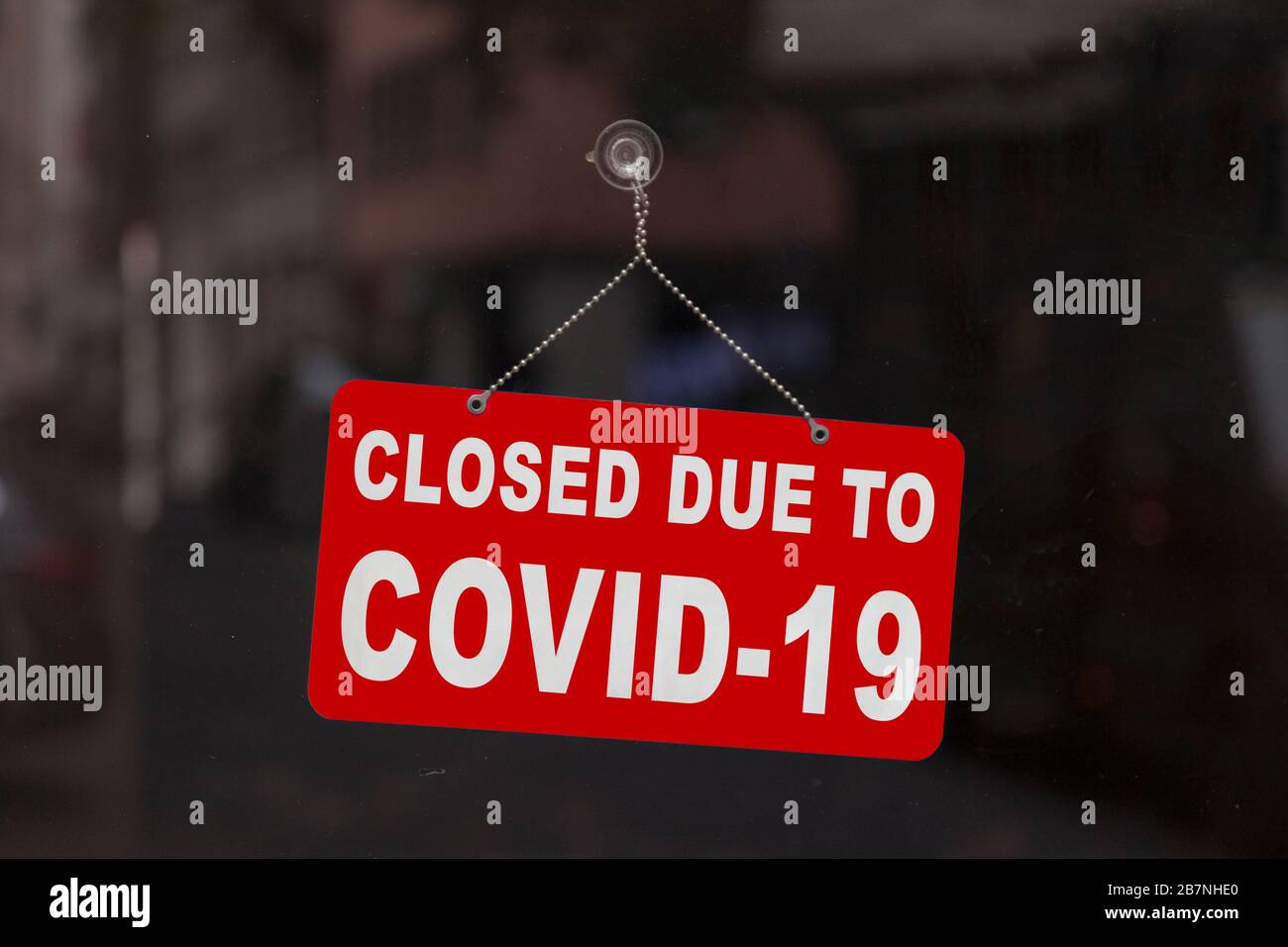 Nahaufnahme auf einem roten, geschlossenen Schild im Fenster eines Shops, das die Meldung "geschlossen aufgrund von Covid-19" anzeigt. Stockfoto