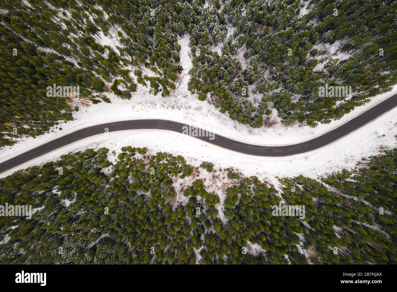 Flug über die Winterberge mit Straßenserpentin und verschneiten Wald. Draufsicht. Landschaftsfotografie Stockfoto