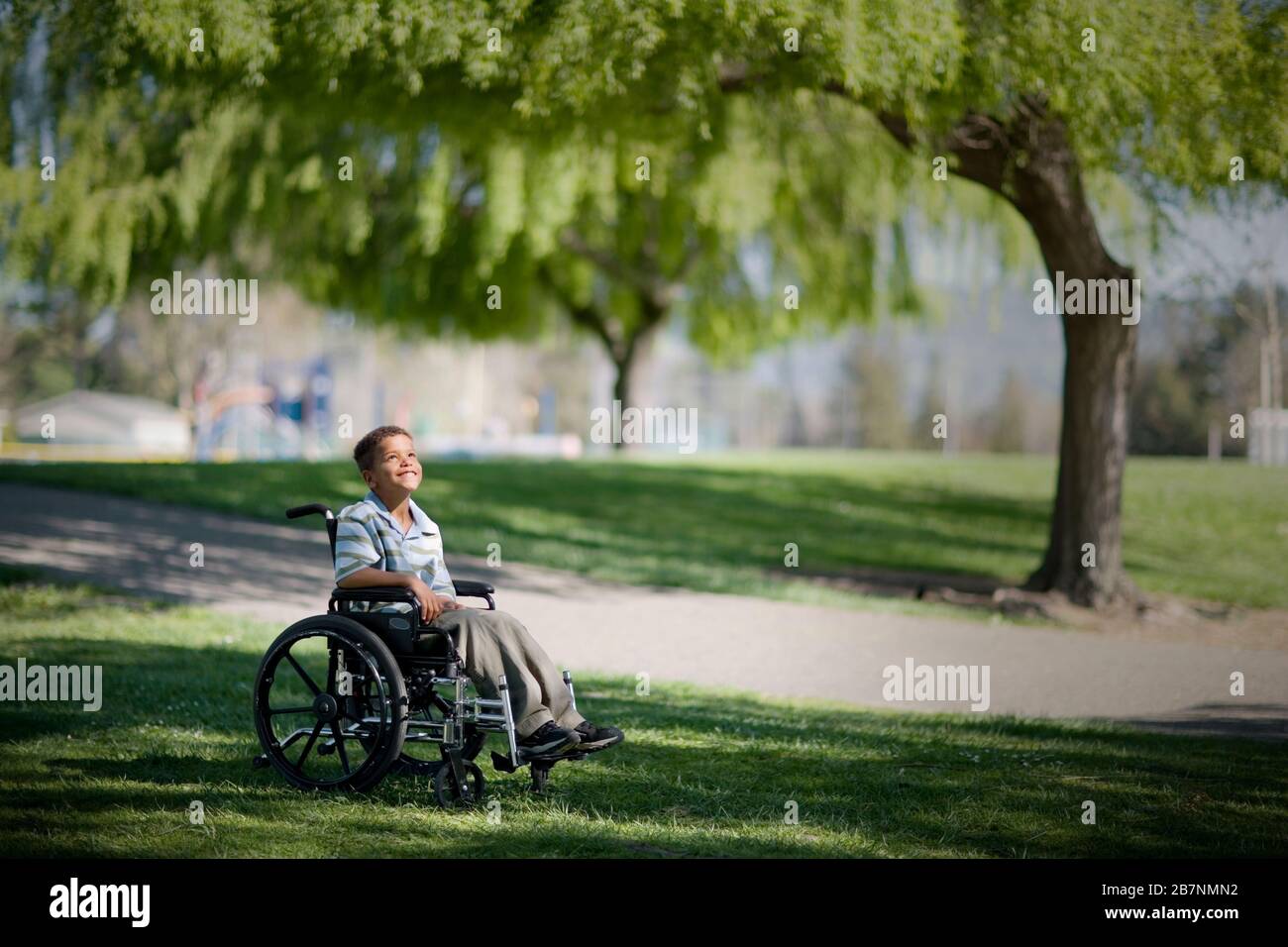 Lächelnde junge Junge sitzt in einem Rollstuhl im Park. Stockfoto