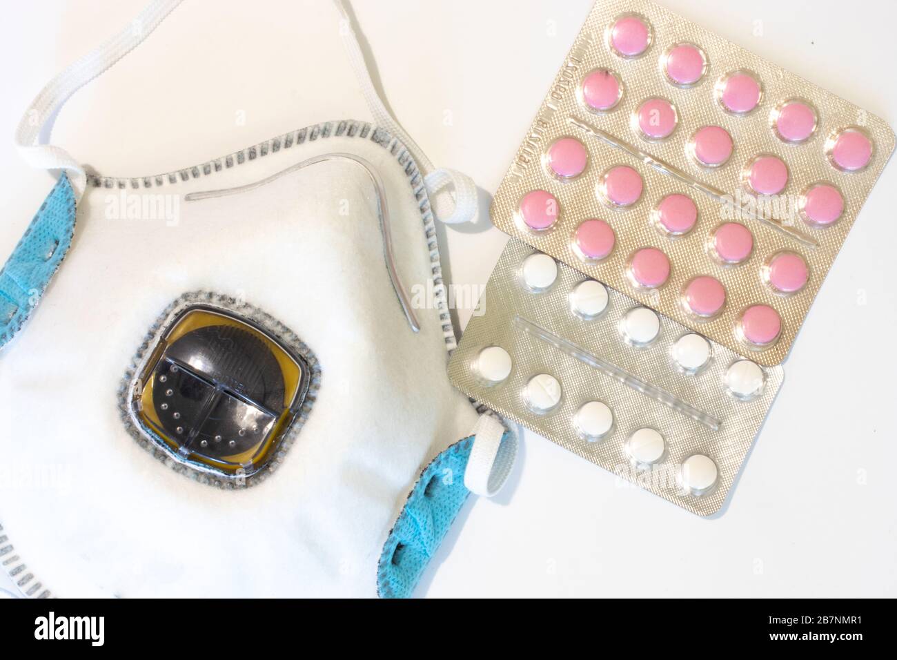 Atemschutzmaske auf weißem Hintergrund mit Tabletten oder Pillen Draufsicht. Medizinische Maske flach gelegt Stockfoto