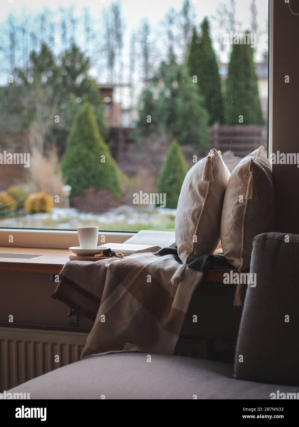 Gemütlicher Platz auf einer Fensterbank zum Lesen und Tagträumen. Frühfrühling, leichter Schnee. Bleiben Sie während der Quarantäne von Covid 19 zu Hause Stockfoto