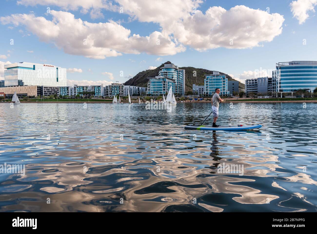 Mann paddeln auf dem Tempe Town Lake vor luxuriösen Eigentumswohnungen am Wasser und Glasgebäuden. Stockfoto