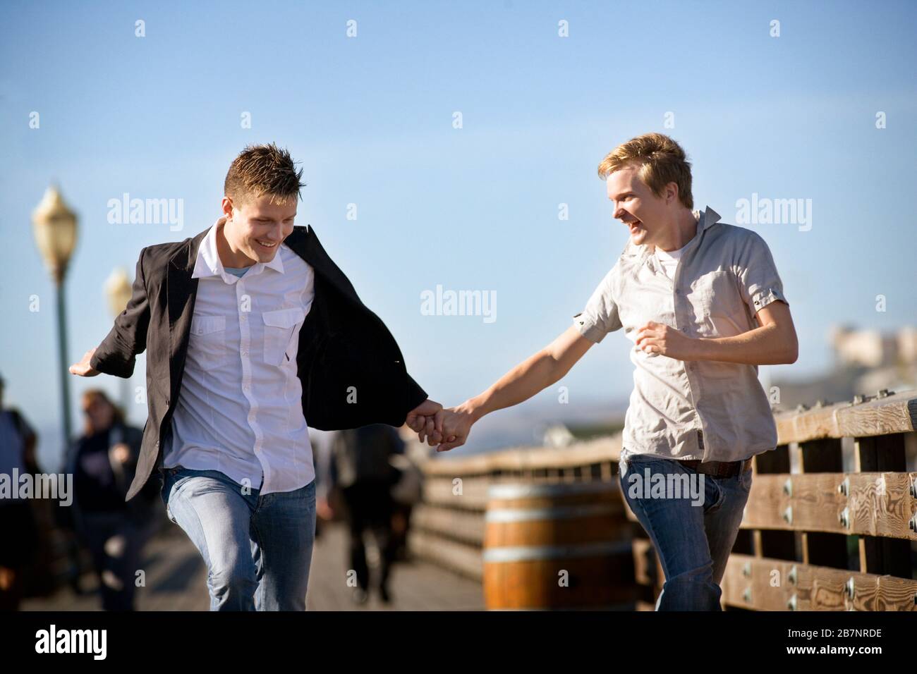 Zwei lächelnde junge homosexuelle Männer laufen zusammen, während sie die Hände halten. Stockfoto
