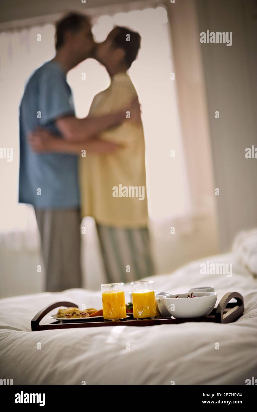 Frühstück auf einem Bett sitzend, während ein Paar küsst. Stockfoto