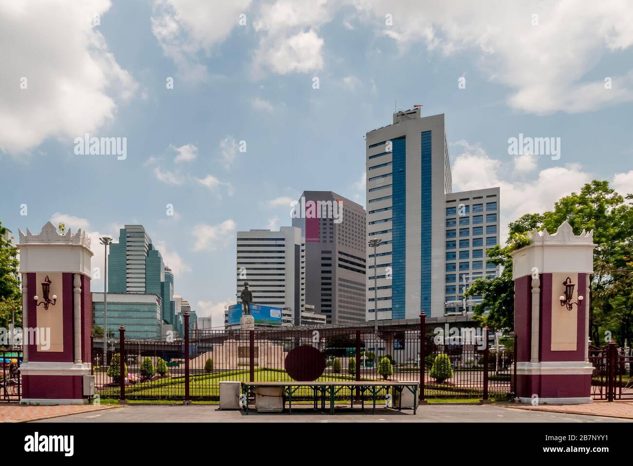 Einer der Eingänge zum Lumphini Park in Bangkok, Thailand, mit dem Denkmal für König Rama VI. Und den Wolkenkratzern von Silom im Hintergrund Stockfoto