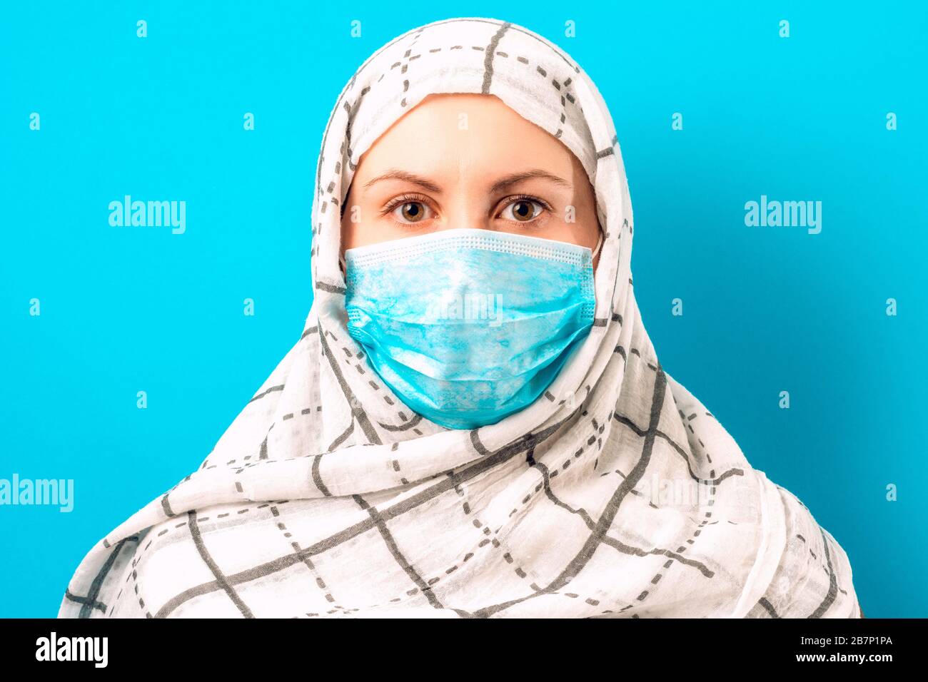 Fröhliche Frau auf blauem Hintergrund in Schal und medizinischer Maske. Stockfoto