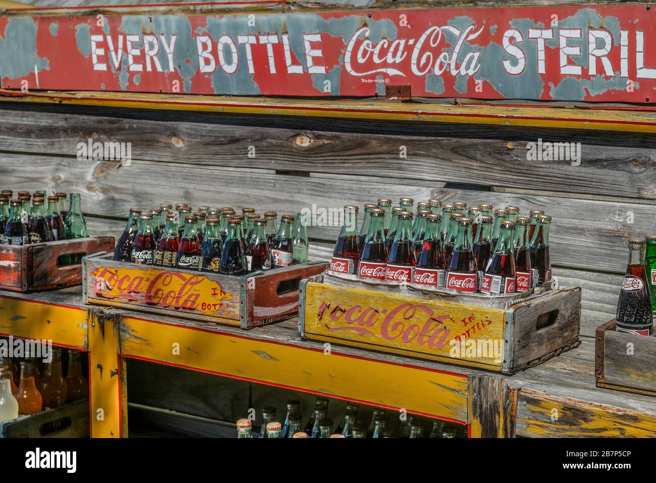 Mehrere Holzkisten mit Vintage-Flaschen von Coca-Cola sind immer noch voll mit Limonade auf einem alten Lieferwagen im Freien ausgestellt Stockfoto