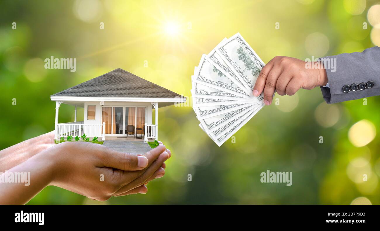 Die Hände eines Kaufmanns Geld und die andere Hand hält ein Haus. Die Idee, Geld zu sparen, um ein Haus zu kaufen Stockfoto