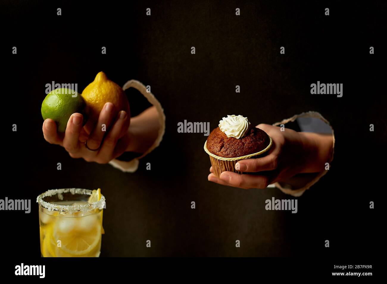 Hand in das Papierloch.Dunkler Hintergrund. Zitrone, Limette und Limonade. Erfrischung. Auf der anderen Seite ist ein Schokoladenkuchen. Die Wahl der richtigen Lebensmittel Stockfoto