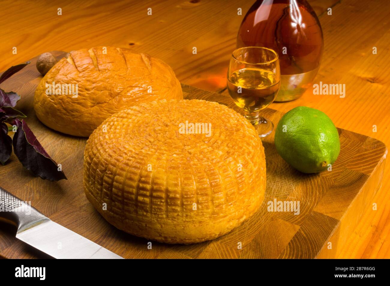 Nationaler Adyghe Käse auf einem Schneidebrett mit einem Messer, Basil, Petersilie, Limette, Sesamöl, Chili Pfeffer, Macadamia-Nüssen und einem Dekanter auf a hausgemacht Stockfoto