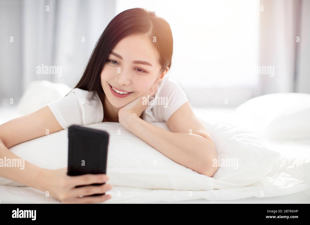 Frau, die im Bett aufwacht und das Smartphone anschaut Stockfoto