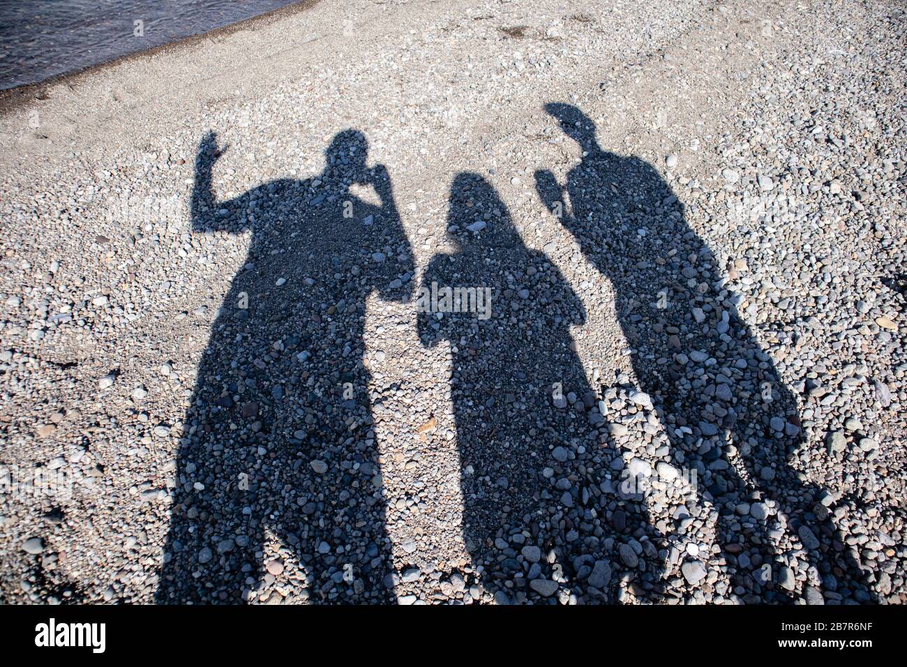 Drei Personen, die mit ihren Smartphones am Strand am Yellowstone Lake in Wyoming Schattenbilder aufnehmen Stockfoto