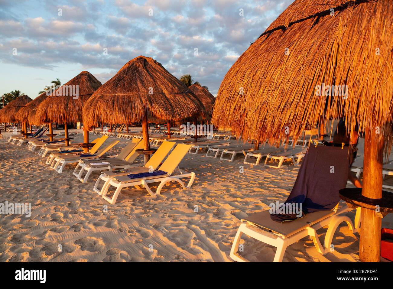 Sonnenaufgang über Lounge-Sesseln und Sonnenschirmen an einem karibischen Strandurlaub an der Riviera Maya in Cancun, Mexiko. Stockfoto