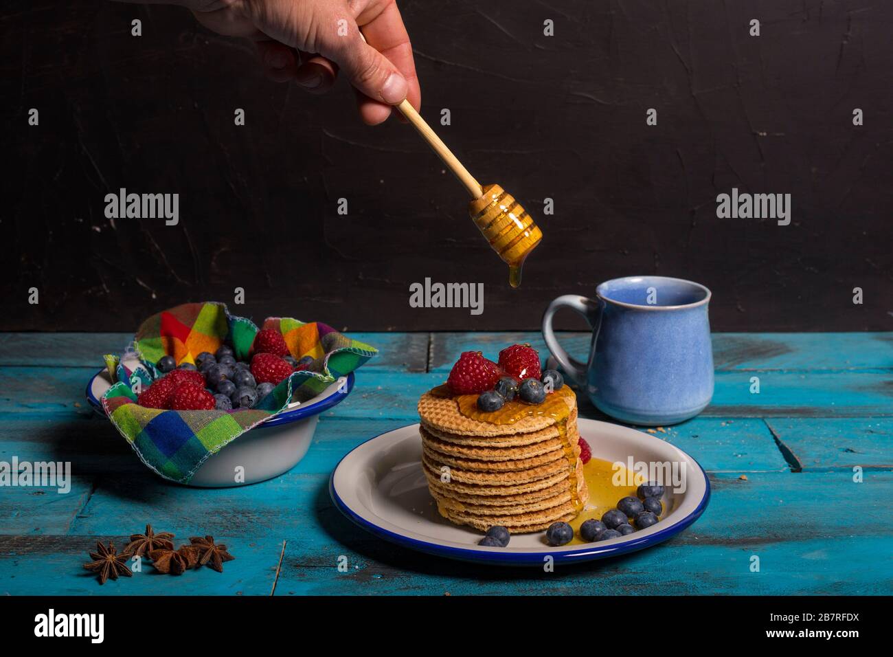Geben Sie Honey mit Honeydewöffel über Waffeln mit Blaubeeren und Himbeeren zum Frühstück auf blauem Holzhintergrund. Frühstückskonzept Stockfoto