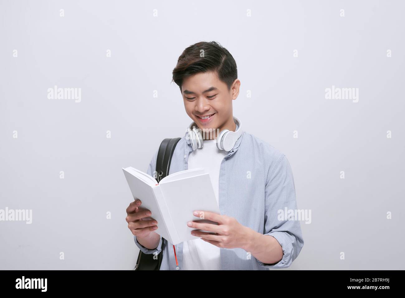 Taillen-Up-Porträt asiatischer Studenten lenkte vom Lesen des Buches ab und schaute mit breitem Lächeln auf die Kamera, isoliert auf weißem Hintergrund Stockfoto