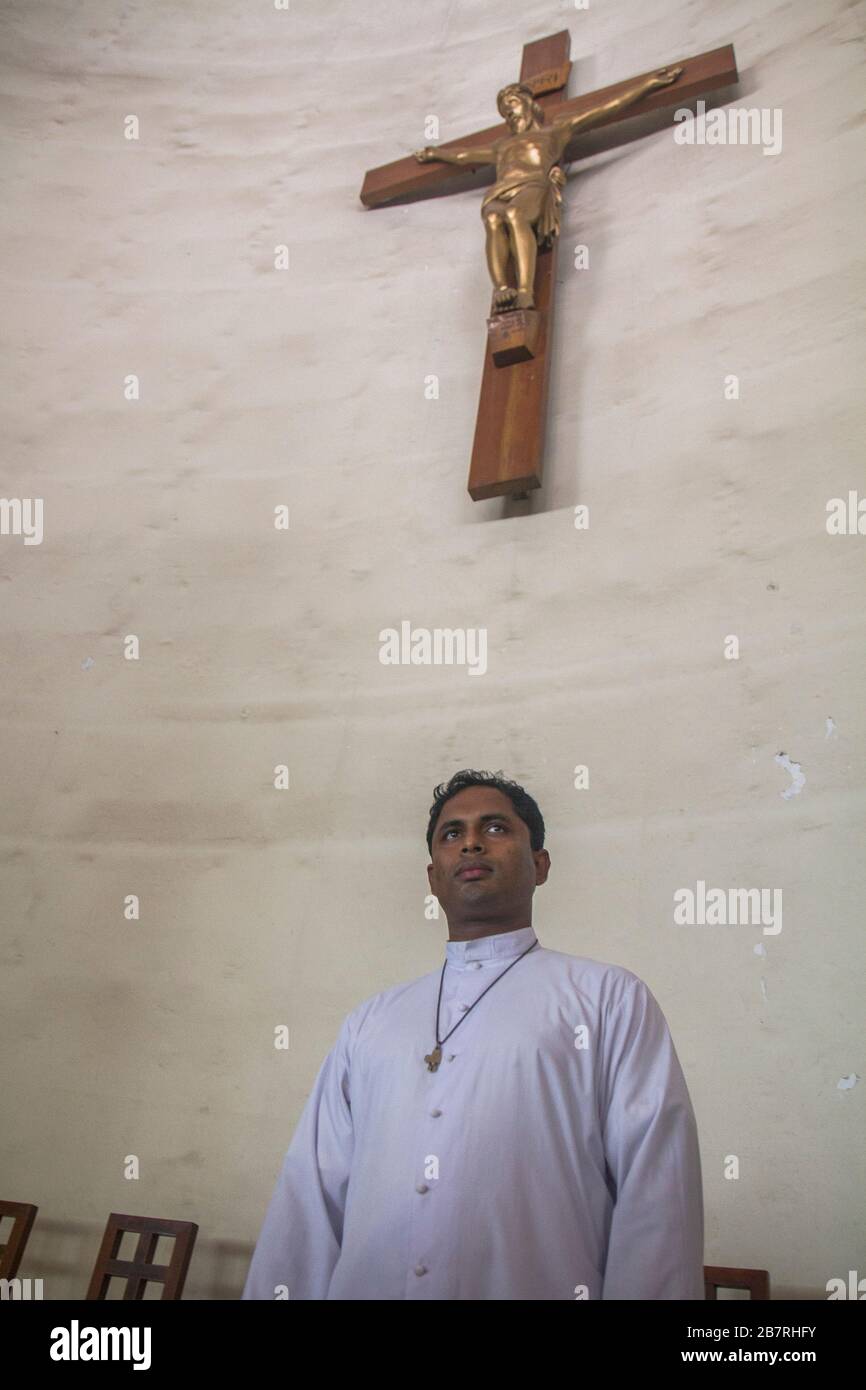 Ein Priester der Tejgaon Kirche mit weißem Kleid, das unter einem Kreuz steht und einen geistlichen Blick nach vorne gibt. Er hat gerade ein paar Kinder getauft. Stockfoto