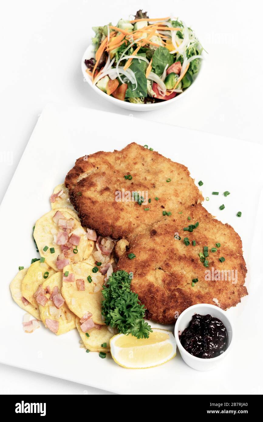 deutsche panierte Schweinefleischschnitzel mit Speck Bratkartoffeln Preiselbeersauce und Salat auf weißem Studiohintergrund Stockfoto