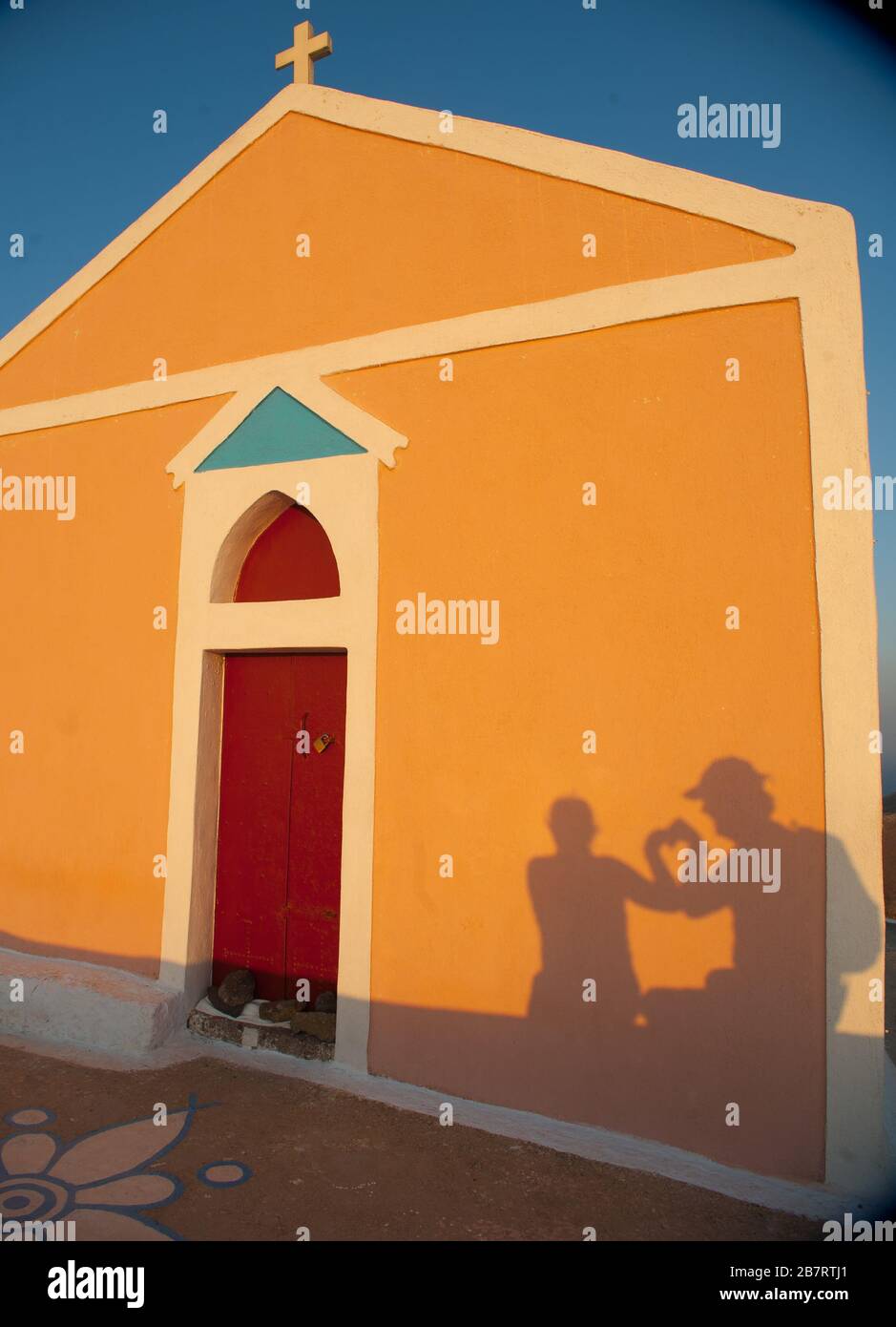 Schatten der touristischen Paar Herz Form mit ihren Händen symbolisieren Zweisamkeit Liebe Romantik und Ehe auf gelben Kirche mit roter Tür Stockfoto