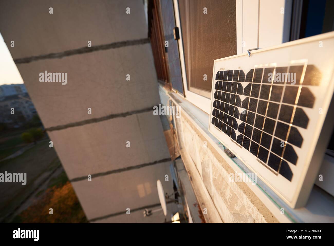 Sonnenkollektor am Fenster eines Hochhauses vor dem Hintergrund eines Schlafbereichs der Stadt bei Sonnenuntergang. Umwandlung von Sonneneinstrahlung in Elektrizität Stockfoto