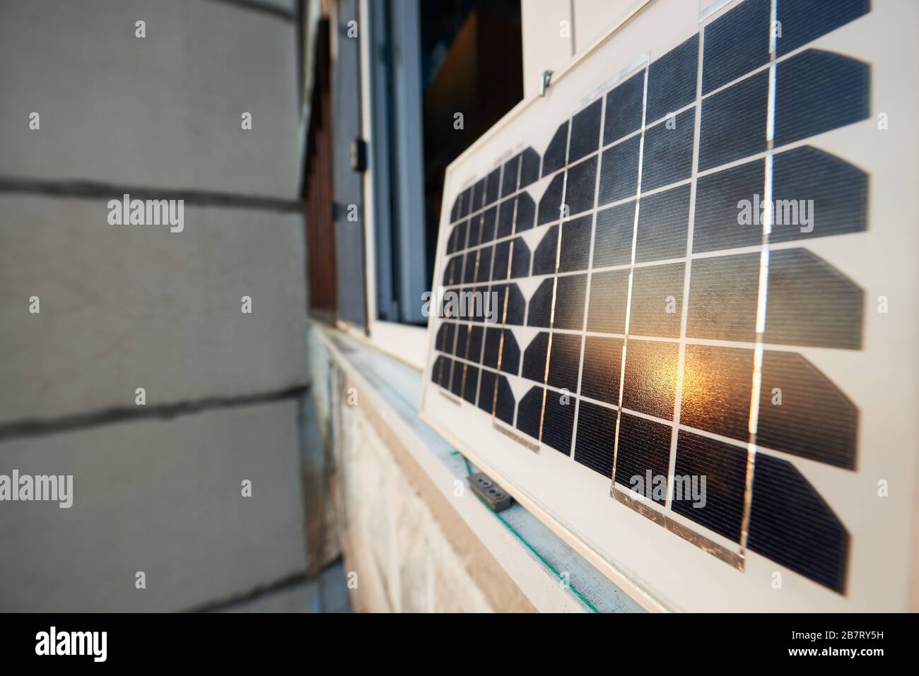 Nahaufnahme eines Solarpanels, das auf einem Fenster eines Hochhauses steht und die Sonne bei Sonnenuntergang reflektiert. Konzept zur Umwandlung von Sonneneinstrahlung in Elektrizität Stockfoto