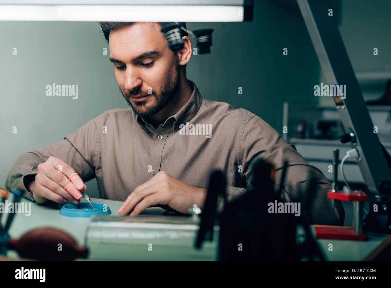 Selektiver Fokus des Uhrmachers, der mit Uhrteilen in der Werkzeugablage am Tisch arbeitet Stockfoto
