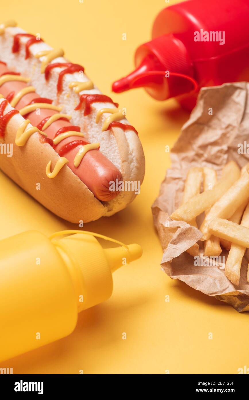 Heißer Hund, pommes frites in Papier und Flaschen mit Ketchup und auf Gelb Stockfotografie -