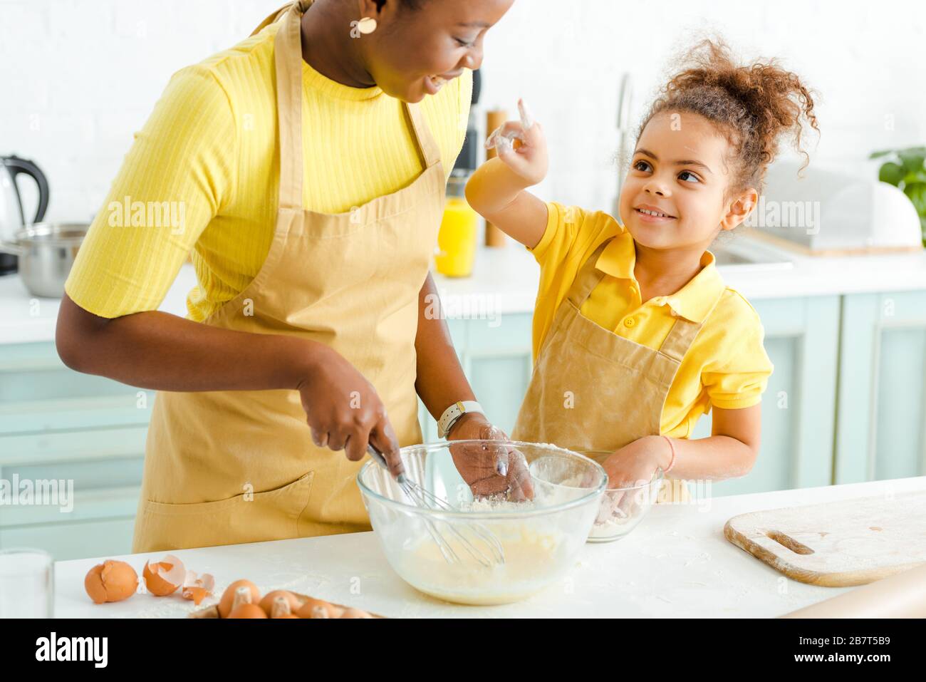 Süßes afroamerikanisches Kind, das mit dem Finger auf die glückliche Mutter in der Küche zeigt Stockfoto