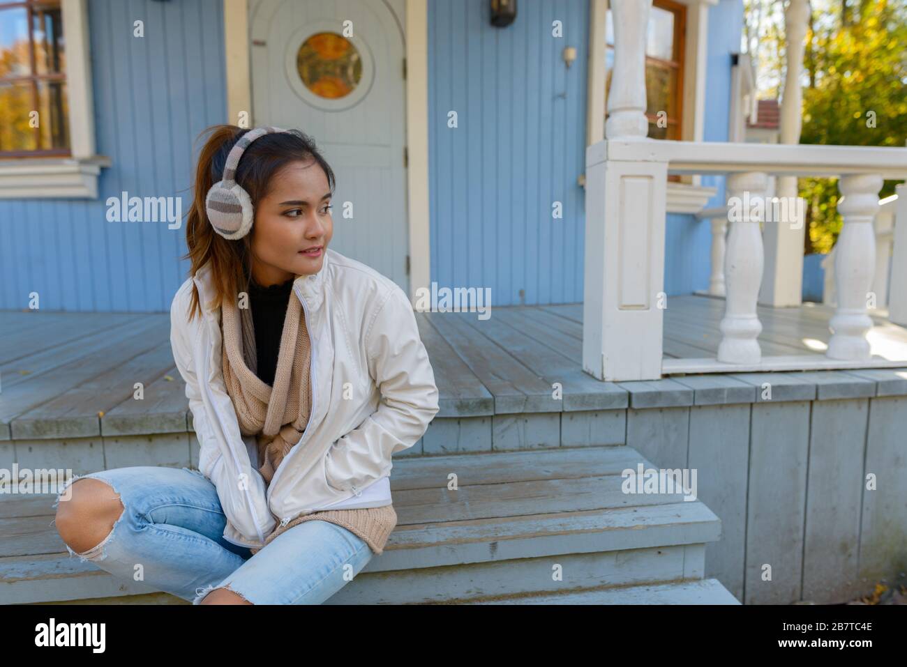 Junge schöne asiatische Frau denkt und sitzt auf einer Treppe des alten blauen Hauses Stockfoto