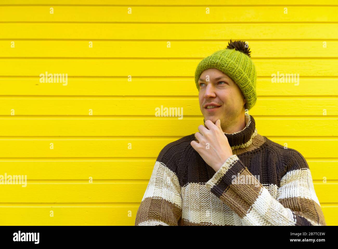 Junger glücklicher gutaussehender Mann, der an die gelbe Holzwand denkt Stockfoto