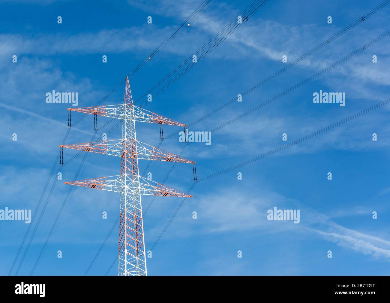 Abgewinkelte Ansicht eines roten und weißen Elektrizitätspylons mit blauem Himmelshintergrund. Stockfoto