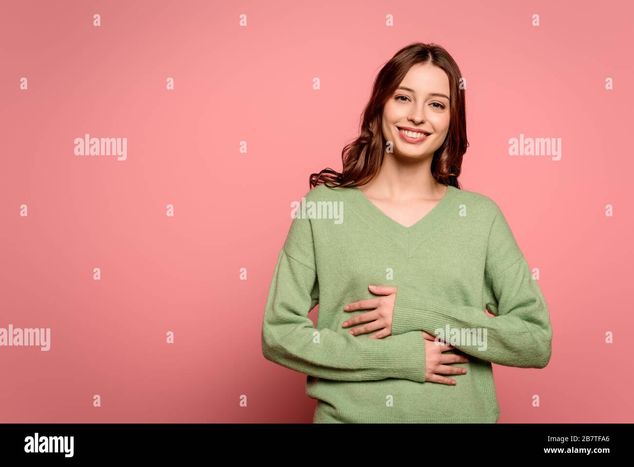 Aufgeregtes Mädchen lacht, während es die Hände auf dem Bauch auf rosa Hintergrund hält Stockfoto