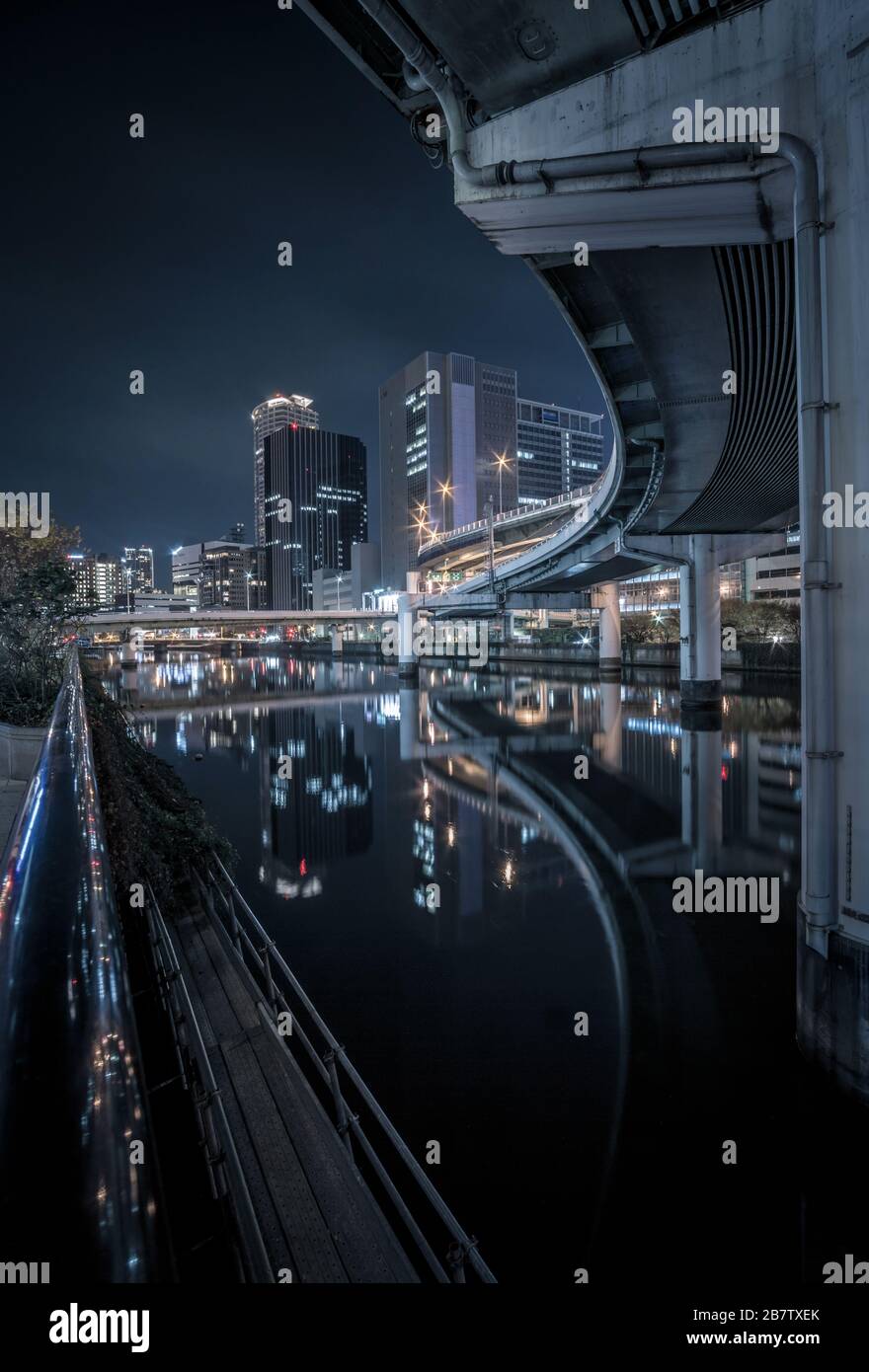 Blick auf die Nacht auf eine erhöhte Autobahn, die den Dojima River in Osaka, Japan, durchquert und im Hintergrund Gebäude hat. Stockfoto