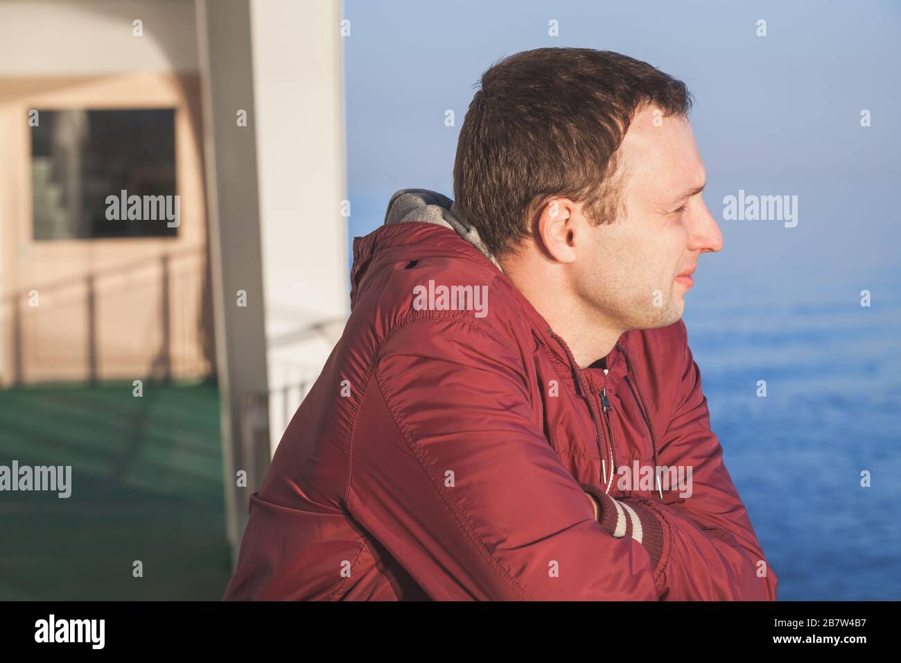 Profil-Nahaufnahme eines jungen kaukasischen Mannes, der in Abendsonne auf einem Wanderdeck eines Kreuzfahrtschiffes steht Stockfoto