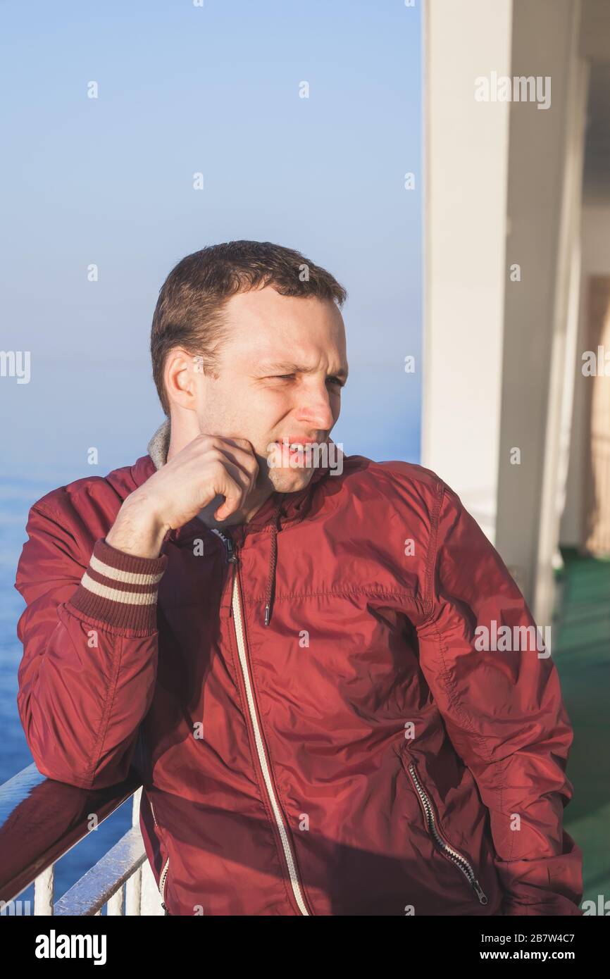 Junger kaukasischer Mann, der bei Sonneneinstrahlung auf einem Wanderdeck eines Kreuzfahrtschiffes steht Stockfoto