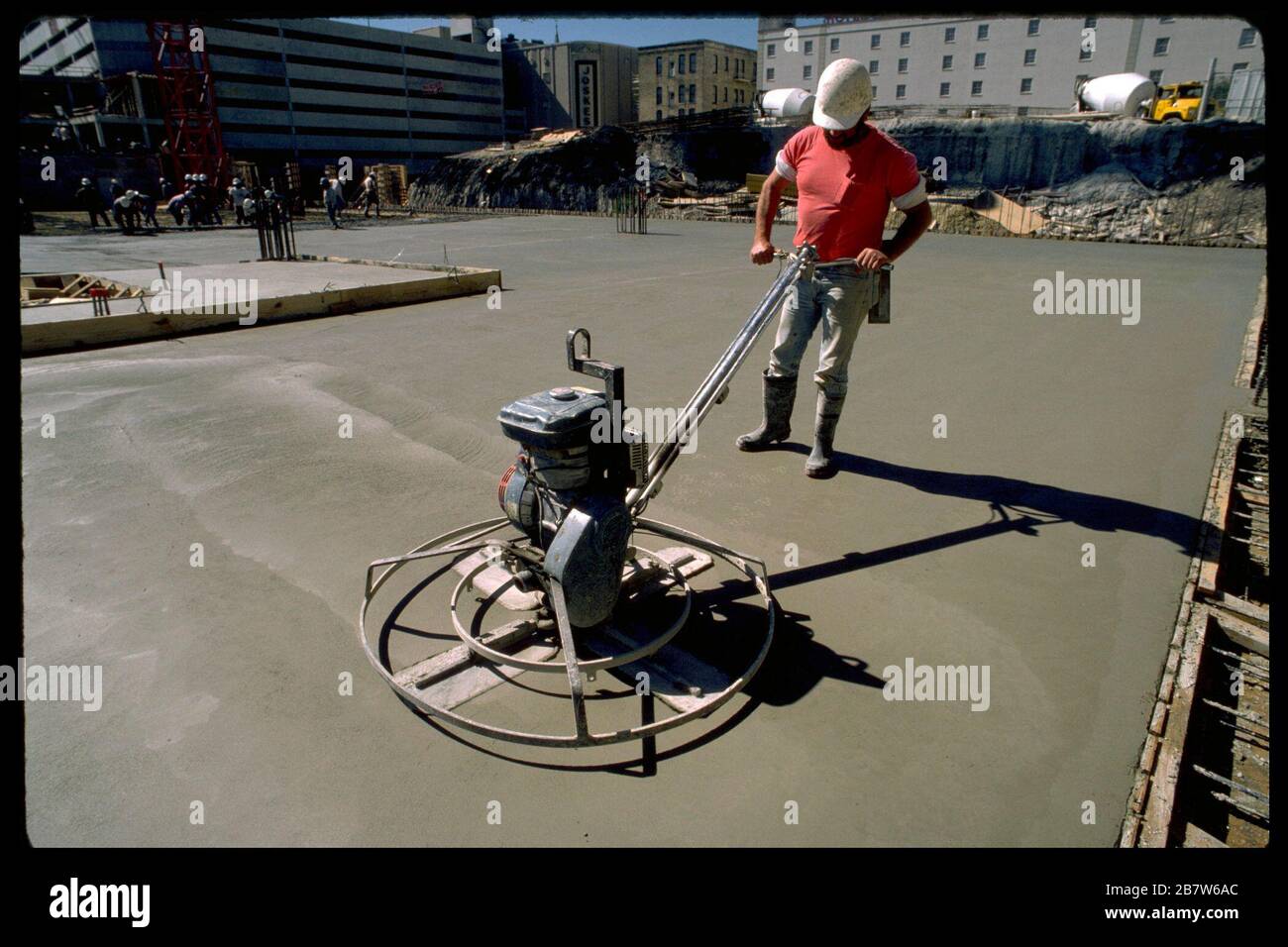 Der Bauarbeiter mit Schutzhelm verwendet eine gasbetriebene Kelle, um Beton auf der kommerziellen Baustelle zu glätten. ©Bob Daemmrich Stockfoto