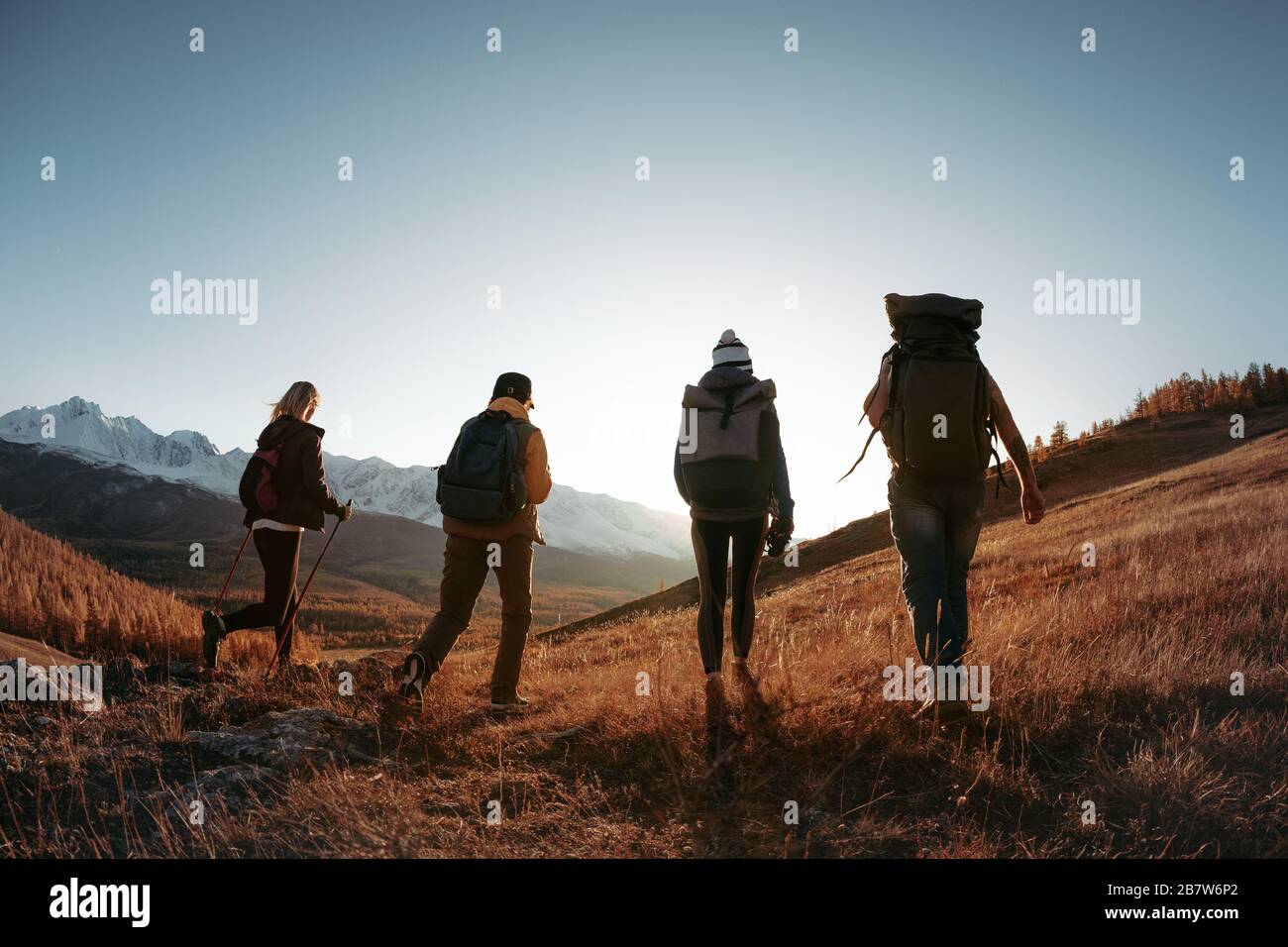 Vier unerkennbare Wanderer oder Rucksackwanderungen mit Rucksäcken in den Bergen bei Sonnenuntergang. Trekking im Bergkonzept Stockfoto