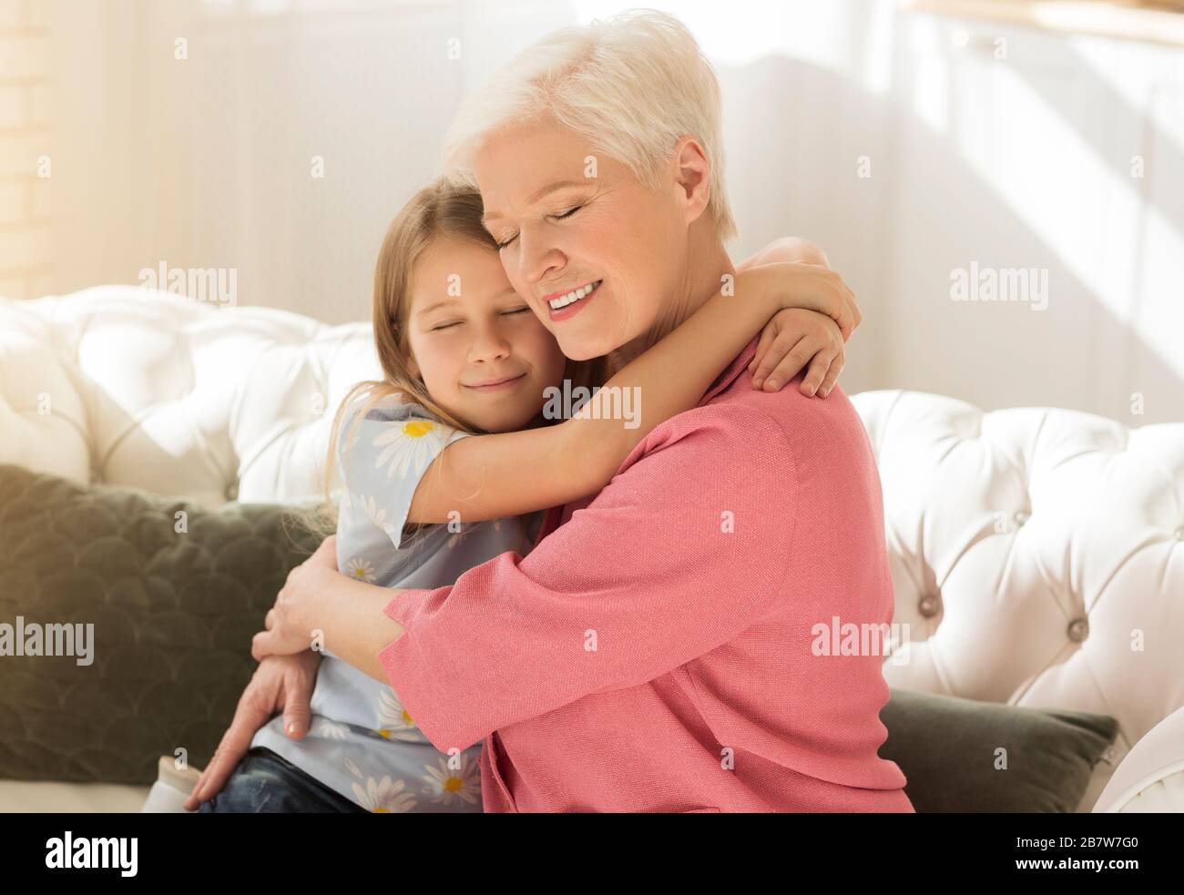 Gealterte Frau mit ihrem Enkelkind umarmte sich im hellen Raum Stockfoto