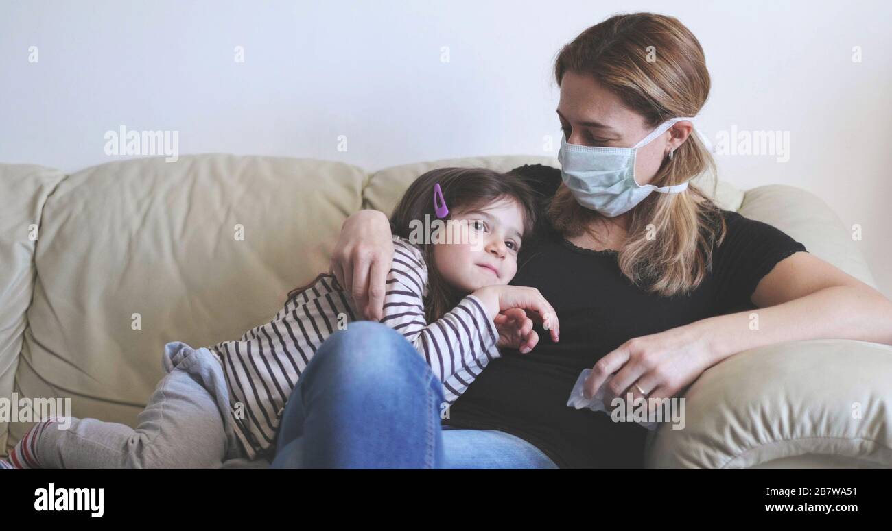 Kranke Mutter mit chirurgischer Maske bleibt mit ihrem Kind auf dem Sofa Stockfoto