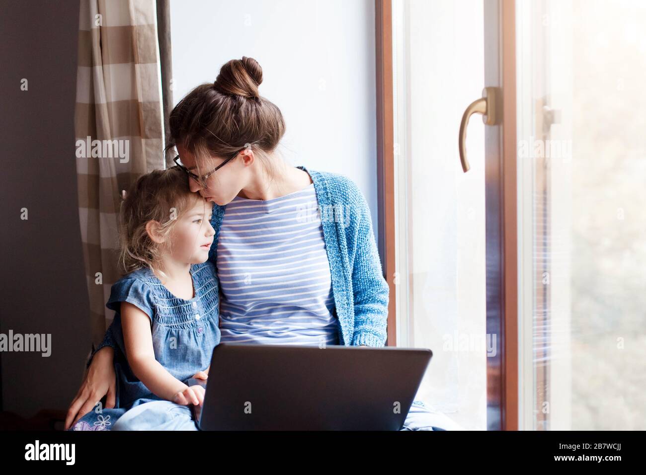 Mutter umarmt und küsst Tochter. Die arbeitende Mutter arbeitet von zuhause aus. Stockfoto