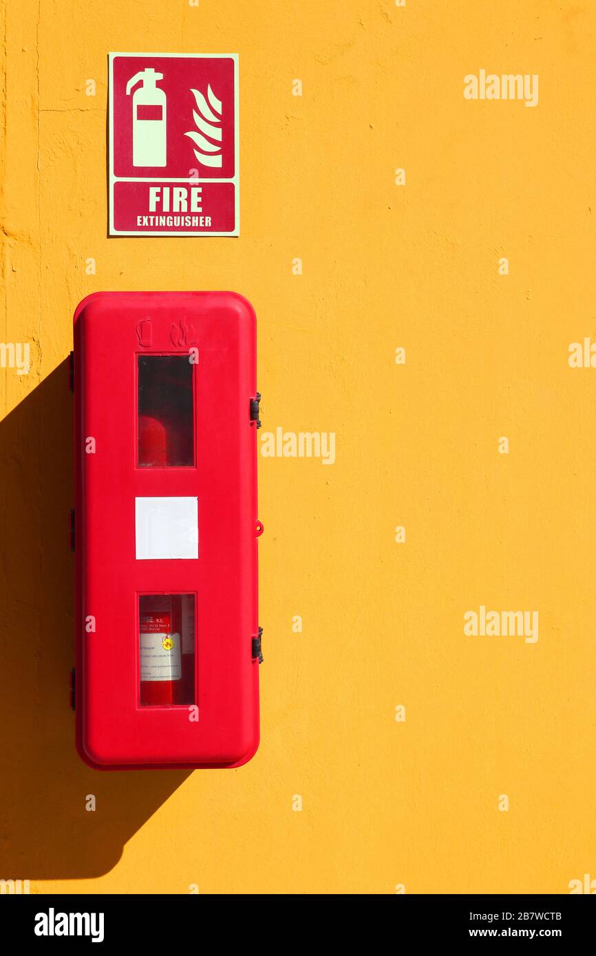 Roter Feuerlöscher an einer gelben Außenwand zur Vorbeugung Stockfoto