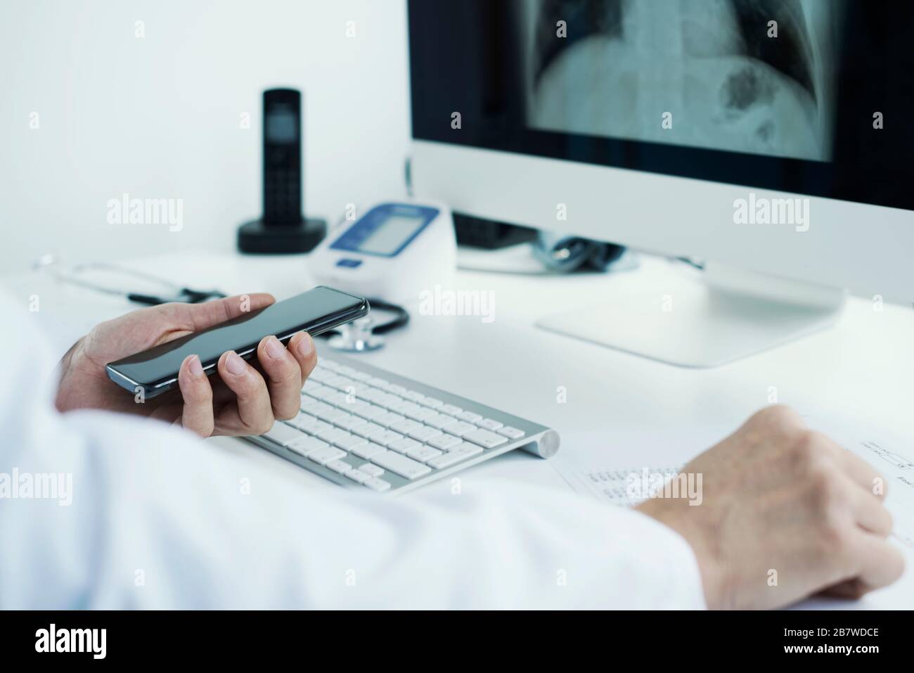 Nahaufnahme eines jungen Arztes, der einen weißen Mantel trägt, an seinem Schreibtisch sitzt und einen Röntgenbild der Brust in seinem Computer überprüft Stockfoto