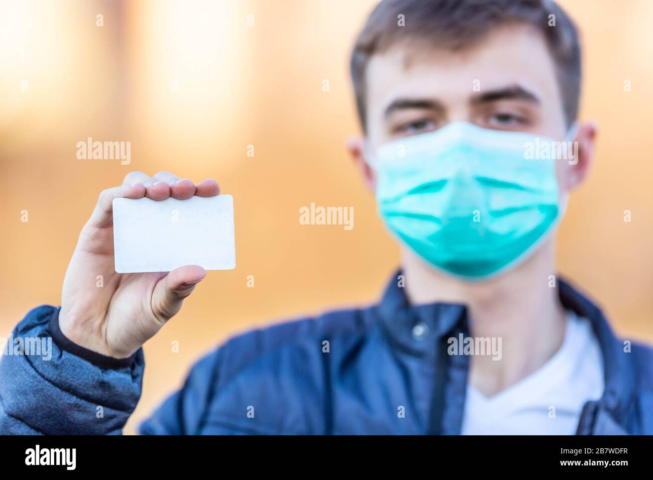 Junger Mann mit Schutzmaske auf dem Gesicht, der eine weiße Karte hält. Schutz vor Virenstaub oder Smog. Coronavirus Covid-19-Konzept. Stockfoto