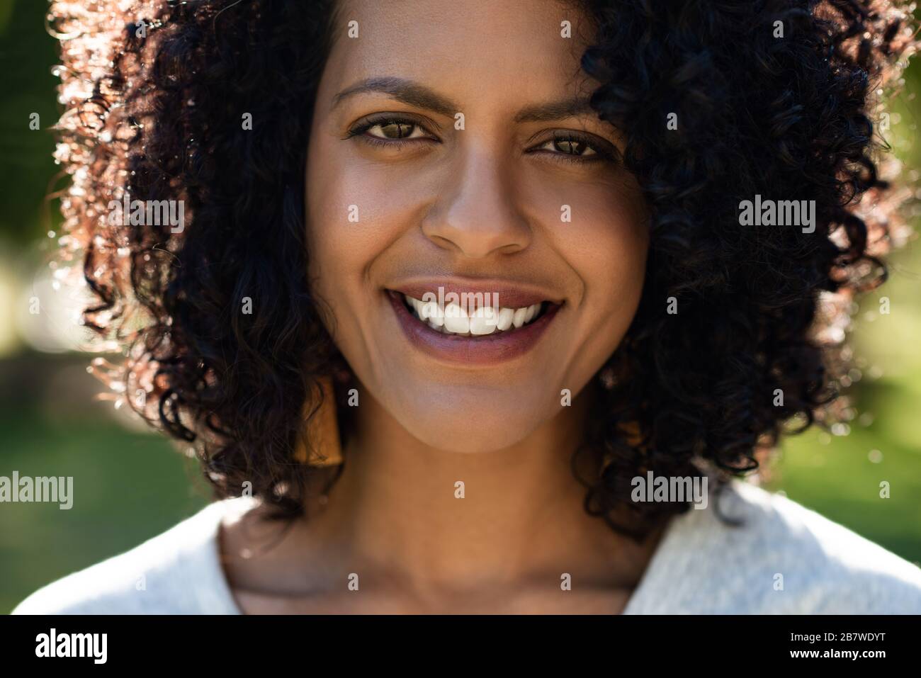 Junge Frau, die im Sommer draußen steht und lächelt Stockfoto
