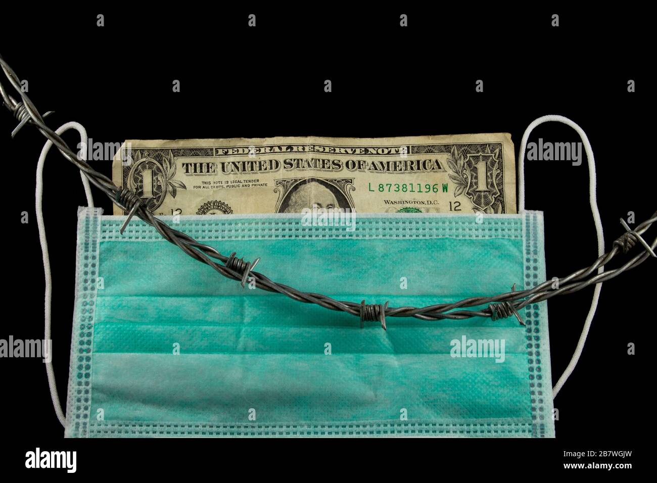 Faltened Dollar Bill hinter einer medizinischen Gesichtsmaske mit Stacheldraht, der oben zum Eingrenzen aufliegt Stockfoto
