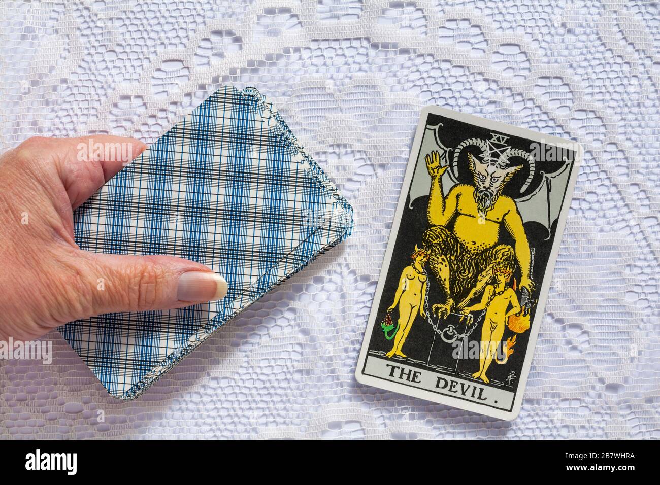 Hand, die Rider Tarot Cards hält, die von Pamela Colman Smith unter Aufsicht von Arthur Edward Waite entworfen wurden, wobei die Devil Tarot Card hochgedreht wurde Stockfoto