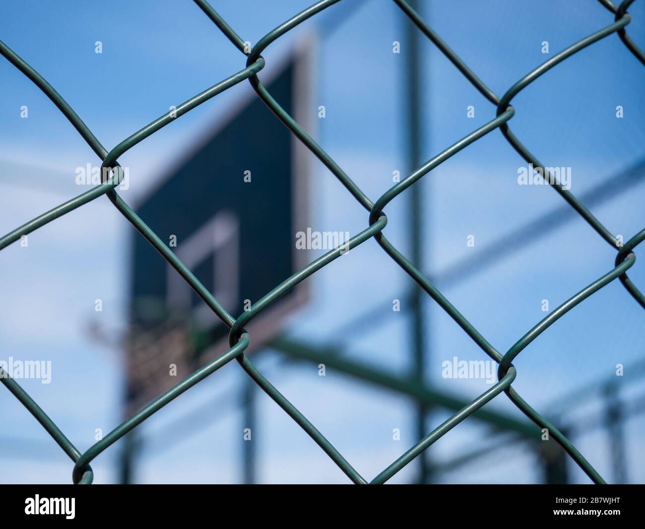 Kabelzaunmuster mit Basketballkorb als Hintergrund. Stahldraht und ein blauer Himmel. Stockfoto