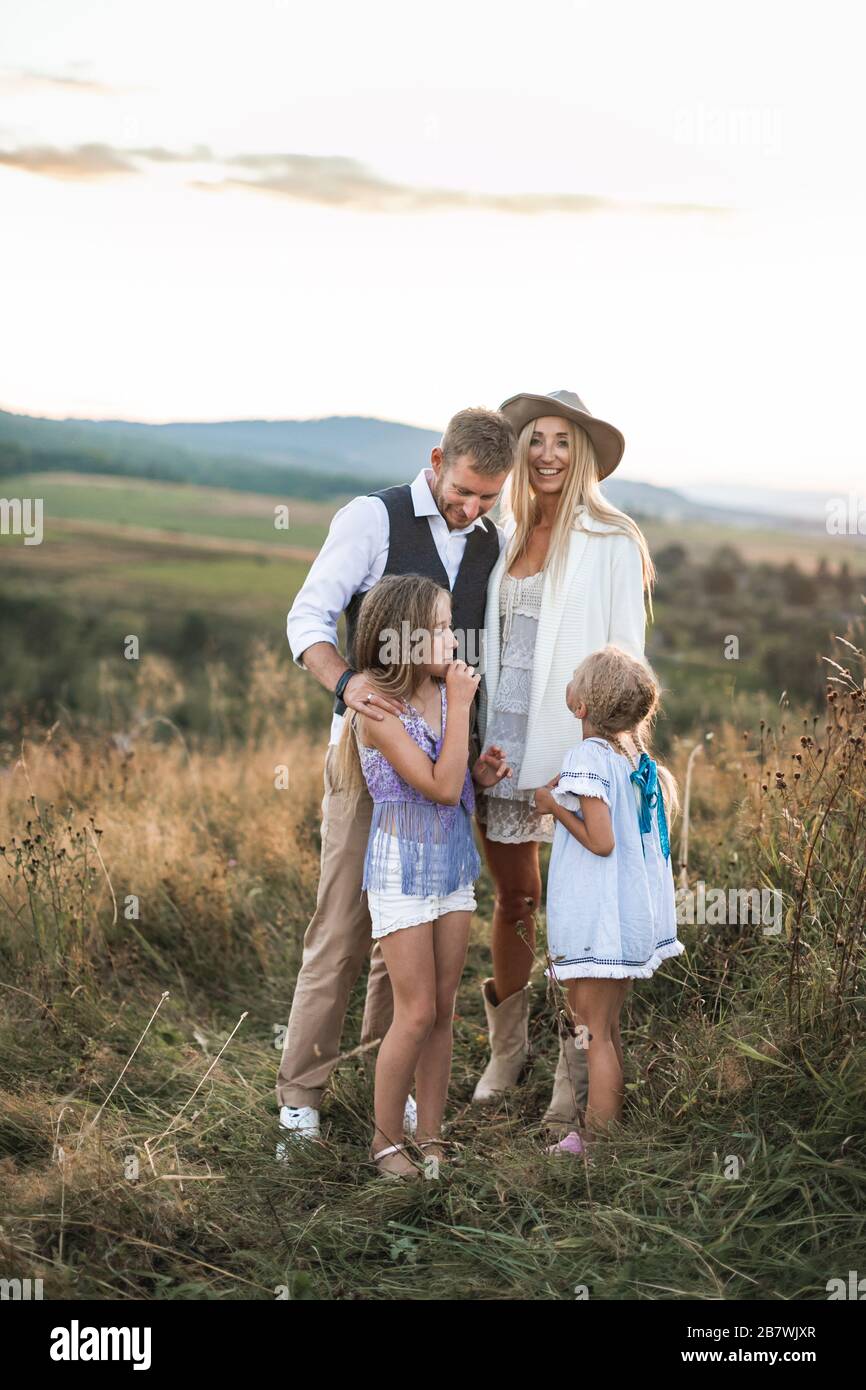 Glücklich lächelnde junge Familie, Vater, Mutter und zwei kleine Töchter, die im Freien Spaß haben und zusammen auf einem wilden Feld stehen. Mutter und Papa sprechen mit Stockfoto