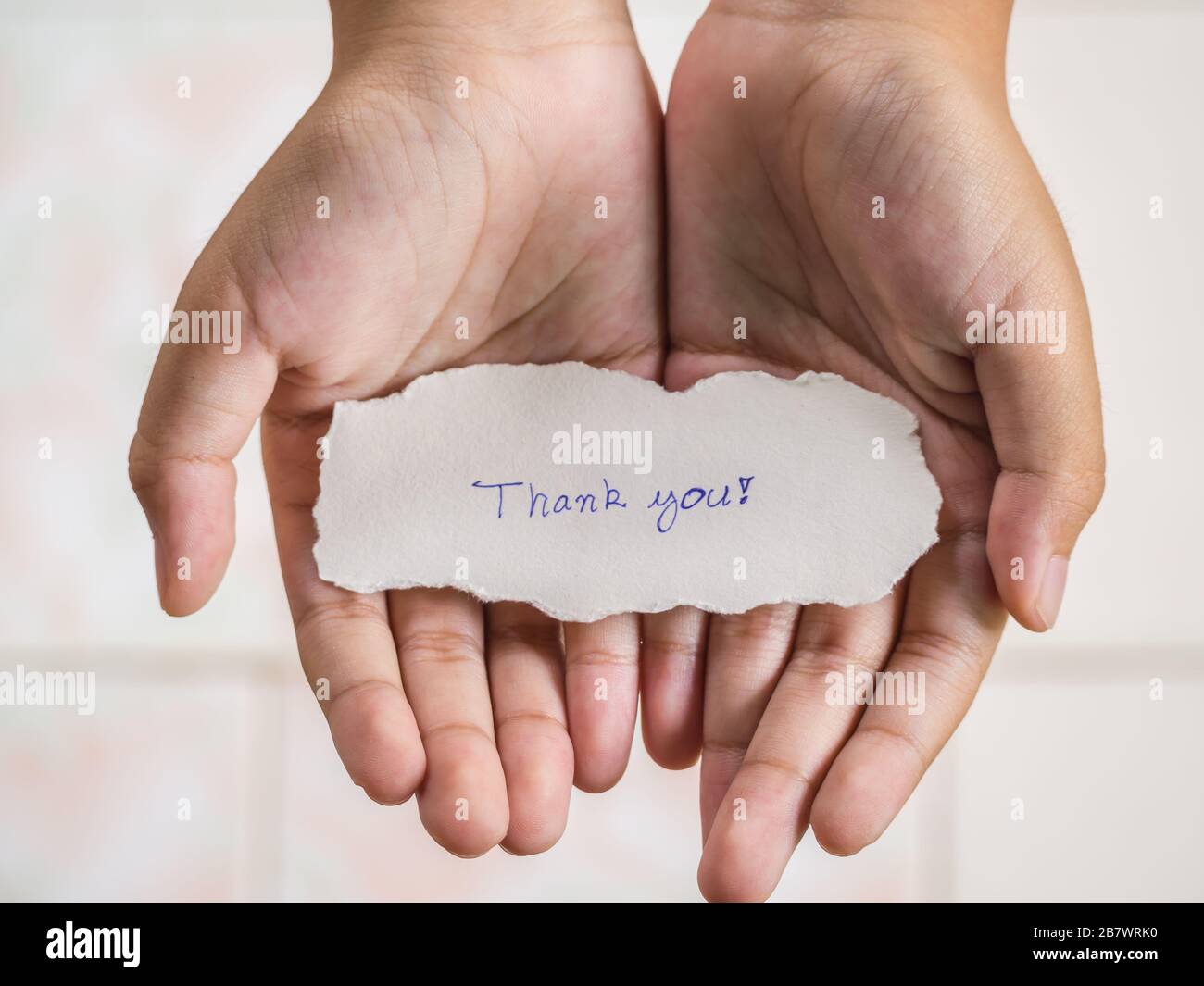 Der Junge, der ein Stück Papier mit dem Wort hält, dankt Ihnen in der Handfläche, die glücklicher ist. Stockfoto