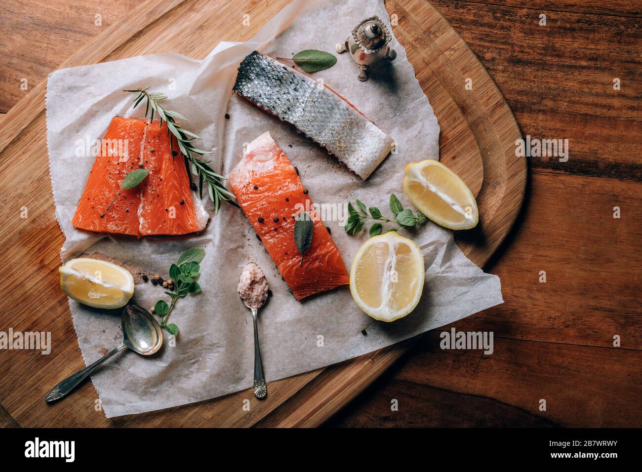 Frischer Rohlachs mit Zitrone, Kräutern und Gewürzen auf Papier auf dem Schneidebrett. Zubereitung von Speisen. Stockfoto